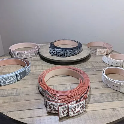 Collection of mariachi belts in assorted colors including black, gold, white, blue, red, and pink