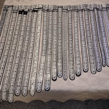 Bulk display of black and silver embroidered mariachi belts laid out in rows