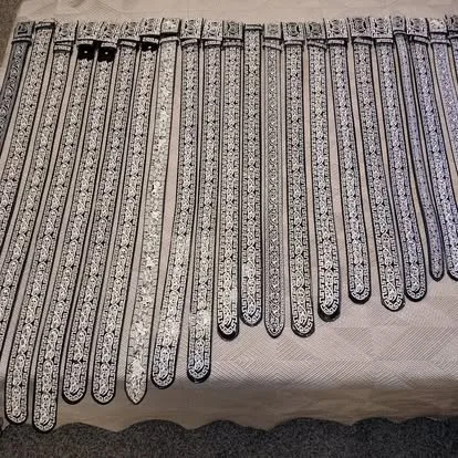 Bulk display of black and silver embroidered mariachi belts laid out in rows