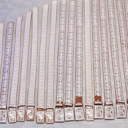 Bulk display of white and gold embroidered mariachi belts with decorative buckles