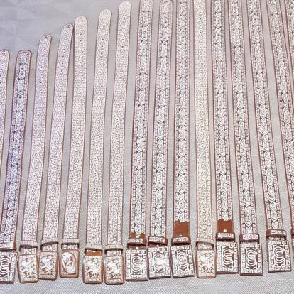 Bulk display of white and gold embroidered mariachi belts with decorative buckles